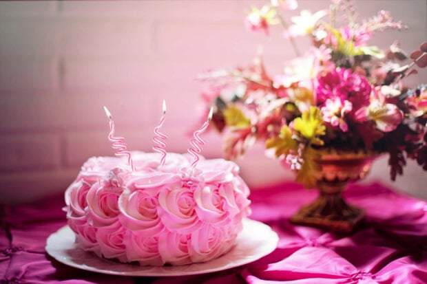 Birthday wallpaper featuring a beautiful pink rose-decorated cake with three spiral candles and a floral bouquet in the background