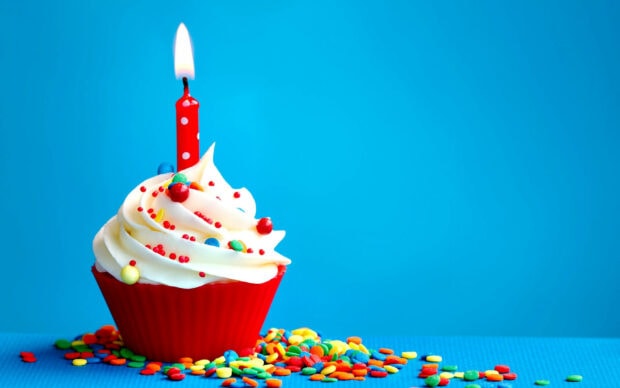 A minimalist birthday wallpaper featuring a single red cupcake with white frosting and a lit candle against a bright blue background