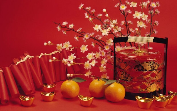 A festive Chinese New Year wallpaper featuring blooming cherry blossoms, oranges, golden ingots, and traditional gift boxes on a red background