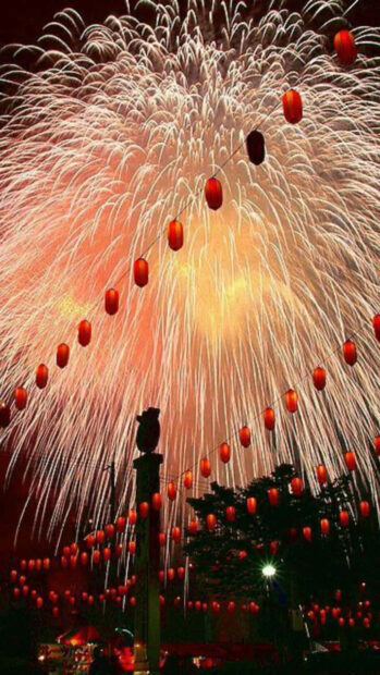 A dazzling Chinese New Year wallpaper showcasing vibrant fireworks exploding behind strings of traditional red lanterns