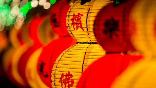 A vibrant Chinese New Year wallpaper featuring a row of glowing red and yellow lanterns with bokeh lights in the background