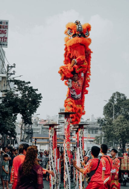 Chinese New Year Wallpaper featuring a vibrant orange lion dance performance on poles in a busy street