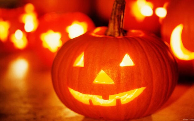 A classic carved jack-o'-lantern glowing warmly in the foreground makes a traditional Halloween Macbook wallpaper