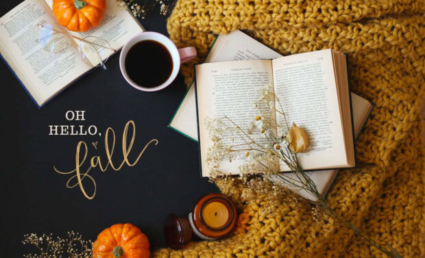 A cozy fall desktop wallpaper flat lay featuring books, a coffee mug, glasses, small pumpkins, and a yellow knitted blanket