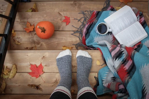 Cute Disney Halloween wallpaper displaying a cozy autumn scene with feet in socks, a small pumpkin, a book, and fall leaves on wooden stairs