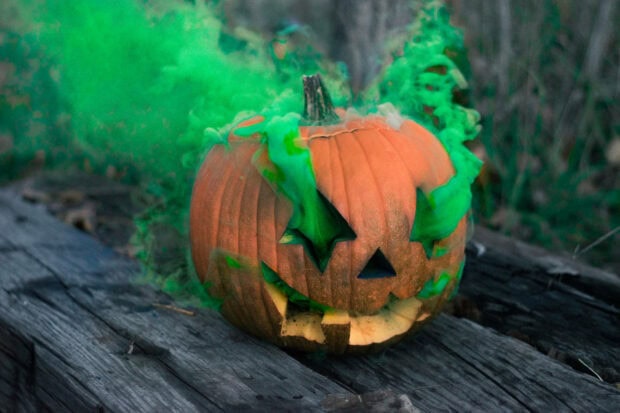 Cute Disney Halloween wallpaper showing a carved pumpkin with green smoke emerging from it on a rustic wooden surface