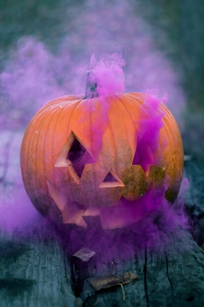 A Cute Disney Halloween Wallpaper showcasing a carved pumpkin emitting vibrant purple smoke on a rustic wooden surface