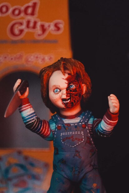 A cute Halloween wallpaper showing a Chucky doll with a damaged face holding a knife, suitable for mobile