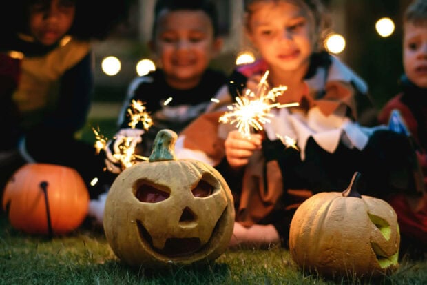A cute Halloween wallpaper featuring children playing with sparklers next to carved pumpkins at night