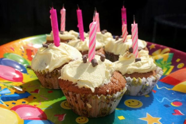 Delicious frosted cupcakes with lit pink candles on a colorful party plate, ideal for a Birthday Wallpaper