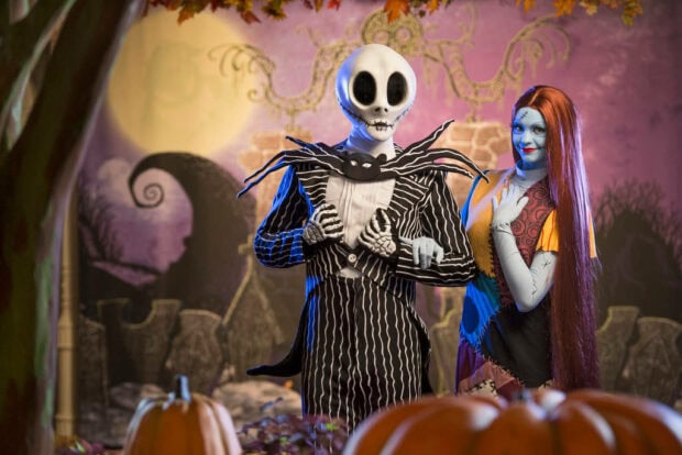A Disney Halloween wallpaper featuring Jack Skellington and Sally standing in a spooky moonlit garden with pumpkins