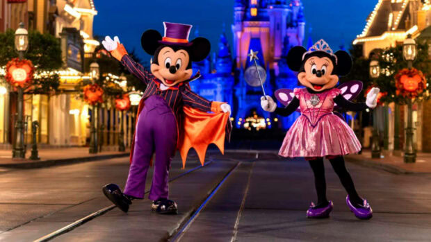 Disney Halloween wallpaper showing Mickey and Minnie Mouse in festive costumes on Main Street with Cinderella Castle at night