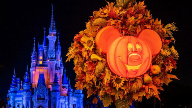 A Disney Halloween wallpaper featuring a Mickey Mouse pumpkin wreath with autumn leaves and Cinderella Castle glowing in the background at night