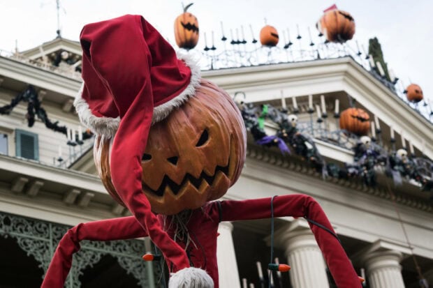 A whimsical Disney Halloween Wallpaper featuring a pumpkin scarecrow wearing a red Santa hat, standing in front of a spooky mansion decorated for Halloween