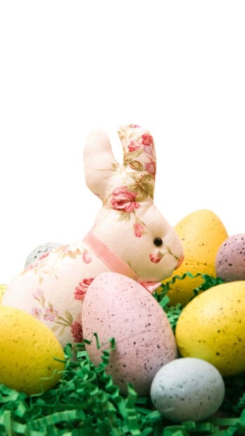 Detailed Easter Bunny wallpaper featuring a floral fabric bunny doll with speckled eggs and green shredded paper