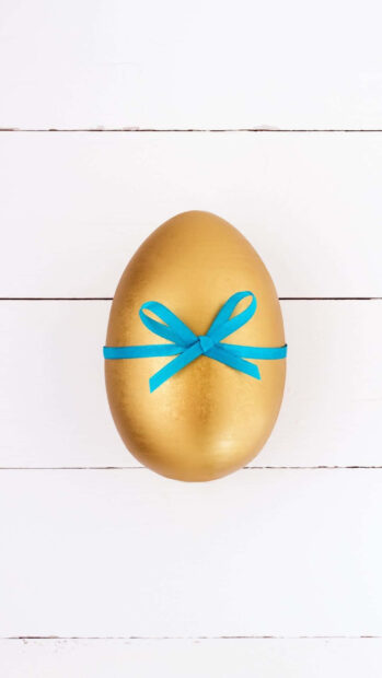 An elegant golden Easter egg wallpaper adorned with a blue ribbon on a white wooden background