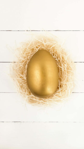 A minimalist Easter Egg wallpaper featuring a shiny golden egg in a delicate straw nest on a clean white wooden background