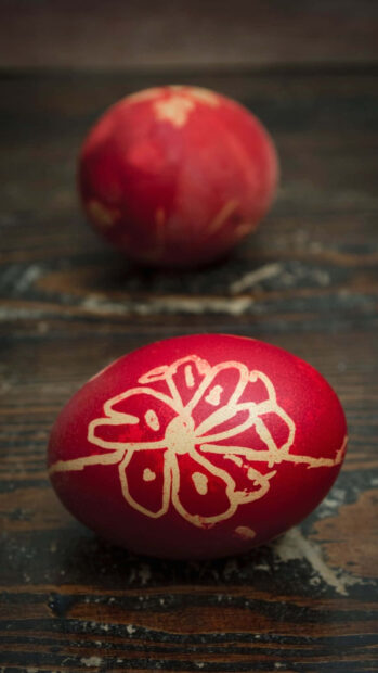 A traditional Easter egg wallpaper showcases a detailed red egg with a golden floral design on a rustic wooden table