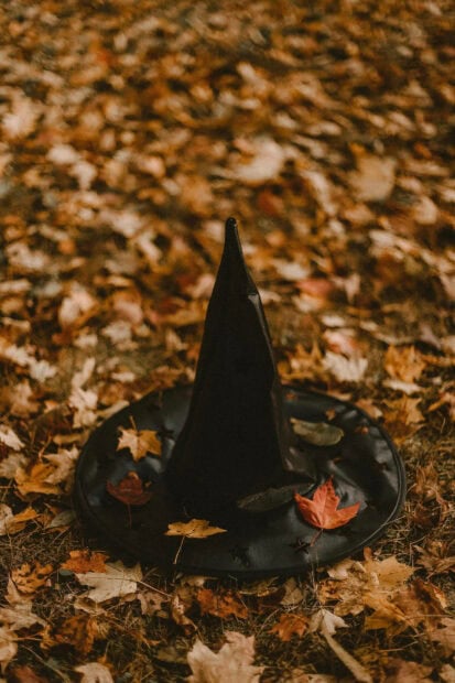 A spooky Fall Aesthetic Iphone Wallpaper featuring a black witch's hat resting on a bed of dry autumn leaves