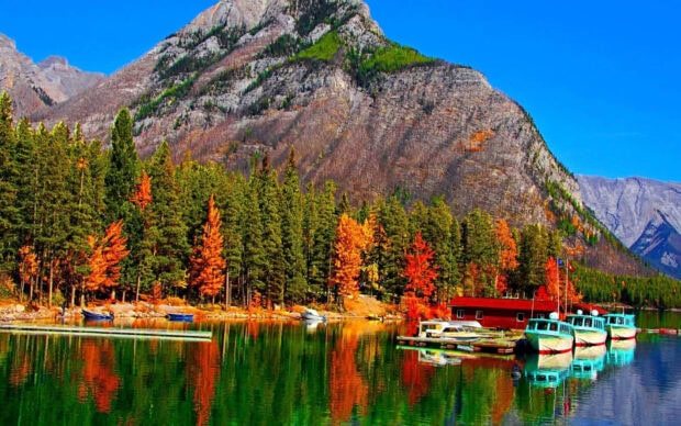 A stunning Fall Colors Wallpaper showcasing a vibrant mountain lake with colorful autumn trees and boats docked by a red building