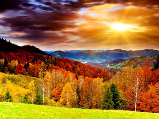 A breathtaking Fall Colors Wallpaper showcasing a panoramic view of autumn mountains and hills under a dramatic sunset sky