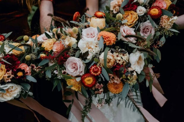 A beautiful Fall Flowers Wallpaper featuring an elegant autumn bouquet with pink, orange, and red roses, dahlias, and eucalyptus leaves