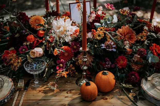 A festive Fall Flowers Wallpaper showcasing a Thanksgiving table setting adorned with vibrant fall flowers, small pumpkins, and tall candles on a wooden table