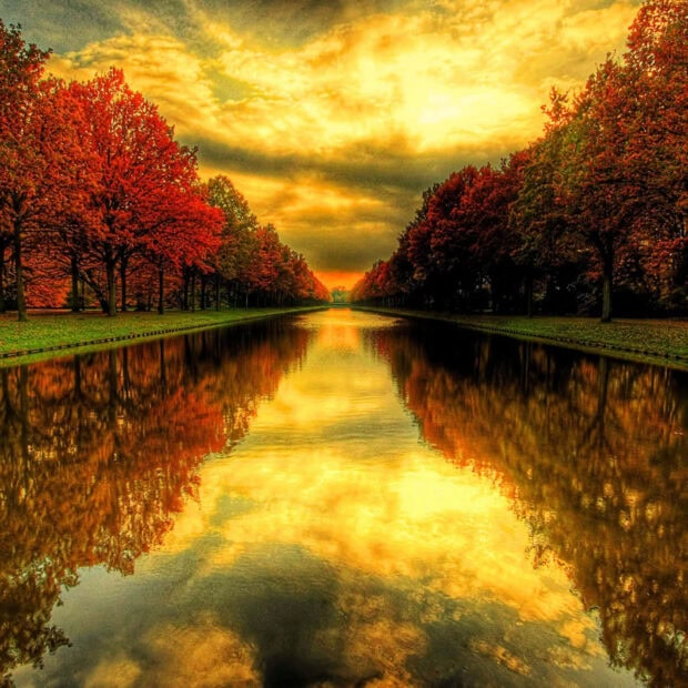 A picturesque canal lined with vibrant autumn trees and their reflections under a golden sky, making a beautiful Fall iPad wallpaper