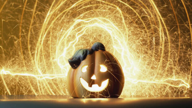 A glowing ceramic jack-o'-lantern with bright golden sparkler light trails creates a festive Halloween Macbook wallpaper