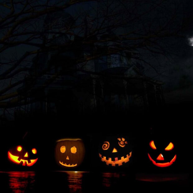 A dark Halloween Ipad Wallpaper featuring four glowing jack-o'-lanterns in front of a spooky haunted house