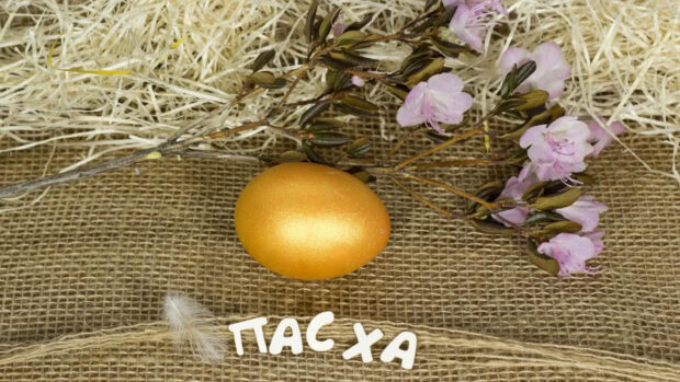 A rustic Easter egg wallpaper showcasing a shiny golden egg, purple flowers, and a feather on burlap fabric