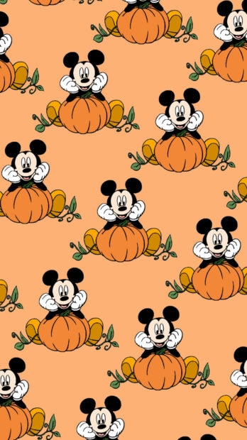 A cute Halloween iPad wallpaper featuring a repeating pattern of Mickey Mouse characters sitting on pumpkins against a light orange background