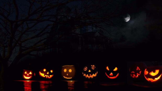 A spooky Halloween Macbook wallpaper showing glowing jack-o'-lanterns in front of a haunted house silhouette under a moonlit sky
