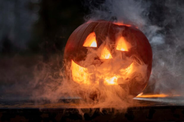 A spooky Halloween Macbook wallpaper featuring a glowing Jack-o'-lantern pumpkin with smoke billowing around it