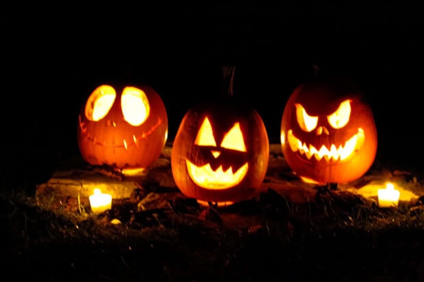 A vibrant Halloween Macbook wallpaper featuring three glowing jack-o'-lanterns with various carved faces illuminated by small candles in the dark