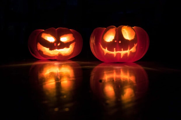 A striking Halloween Macbook wallpaper showcasing two glowing jack-o'-lanterns with their reflections on a dark, glossy surface