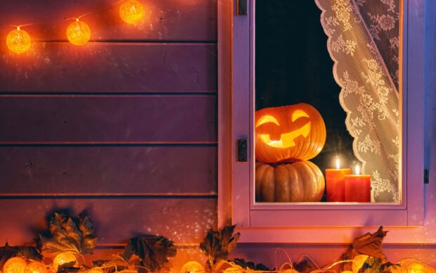 A cozy Halloween Macbook wallpaper showing a carved pumpkin and candles by a window with string lights and autumn leaves outside