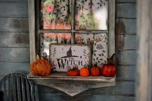 A cozy Halloween Macbook Wallpaper showing a rustic window sill decorated with mini pumpkins and a "The Witch Is In" sign