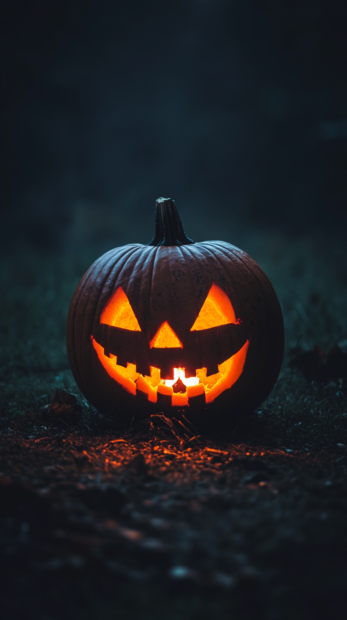 A classic carved Halloween Pumpkin Wallpaper glowing brightly in a dark outdoor setting, perfect for mobile backgrounds