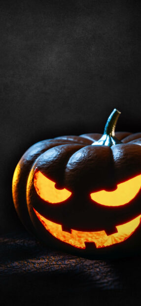 A Halloween Pumpkin Wallpaper showing a close-up of a single glowing jack-o'-lantern with a menacing face against a dark, textured background