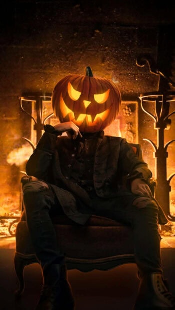 A moody Halloween Pumpkin Wallpaper showing a person with a glowing jack-o'-lantern head sitting in a chair before a warm fireplace