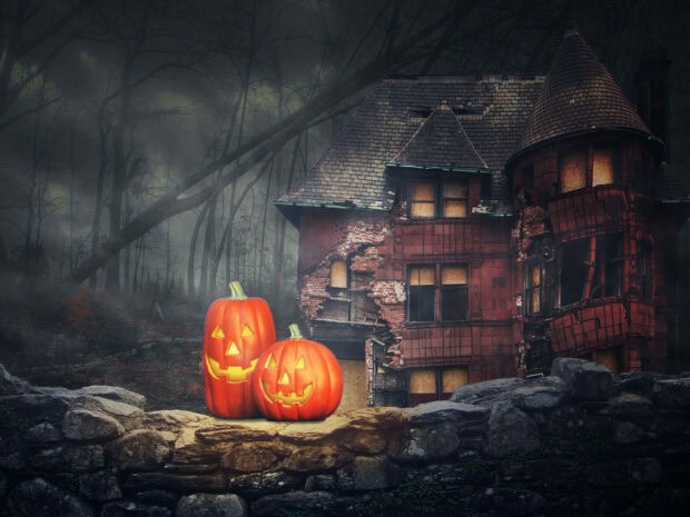 A dark Halloween Pumpkin Wallpaper featuring two glowing jack-o'-lanterns on a stone wall with a haunted mansion in a misty forest