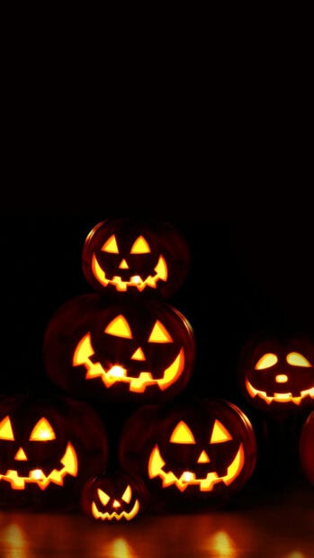 A captivating Halloween Pumpkin Wallpaper featuring a stack of glowing jack-o'-lanterns against a dark background, perfect for mobile devices