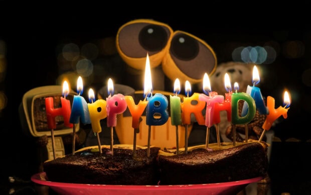 A cozy Birthday Wallpaper showing 'Happy Birthday' candles lit on cake slices with a Wall-E figure in the background