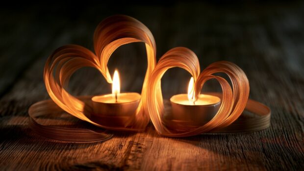 Heart wallpaper showcasing two woven heart shapes with flickering candles on a rustic wooden table
