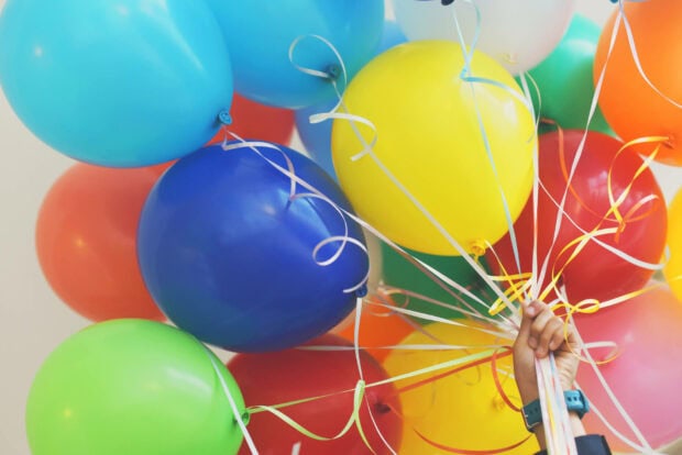 Its My Birthday Wallpaper showing a hand holding a large vibrant bunch of colorful balloons with curling ribbons