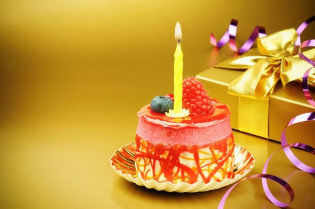 Its My Birthday Wallpaper featuring an elegant individual birthday cake with a lit yellow candle, raspberry, and blueberry on a shimmering gold background with a gift