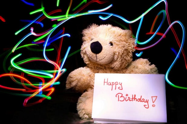 Its My Birthday Wallpaper featuring a fluffy teddy bear holding a 'Happy Birthday!' card with vibrant light trails in the background