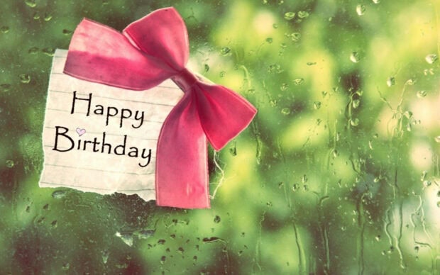 Its My Birthday Wallpaper with a 'Happy Birthday' note and a pink bow taped to a rainy window with a blurred green background