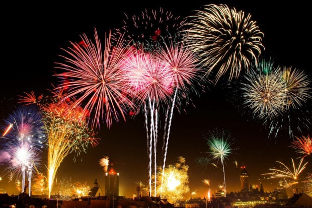 A festive New Years Eve Wallpaper featuring multiple colorful fireworks exploding above a city skyline at night